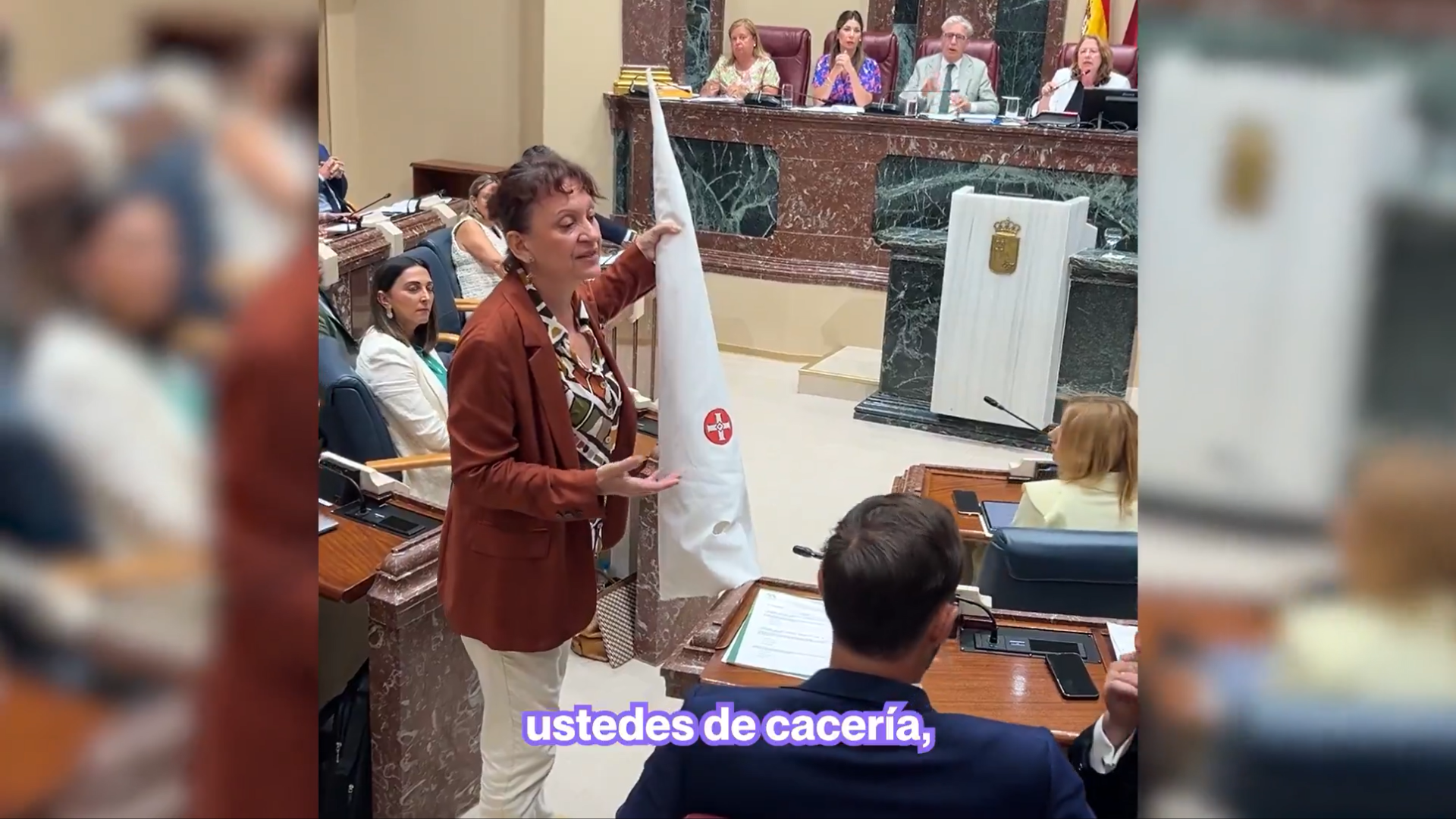 La charo María Marín, portavoz de Podemos en Murcia, coloca un capirote similar al del Ku Klux Klan en los escaños de VOX